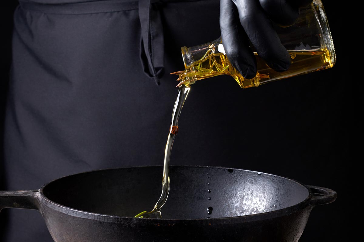 A person cooking with terpenes pours oil on a black cooking pan.