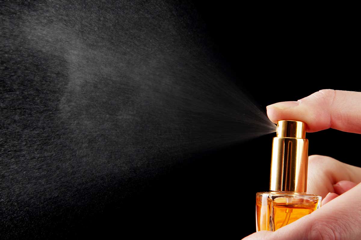 A hand spraying perfume, illustrating the aromatic release of terpenes in perfumes and their volatile nature.