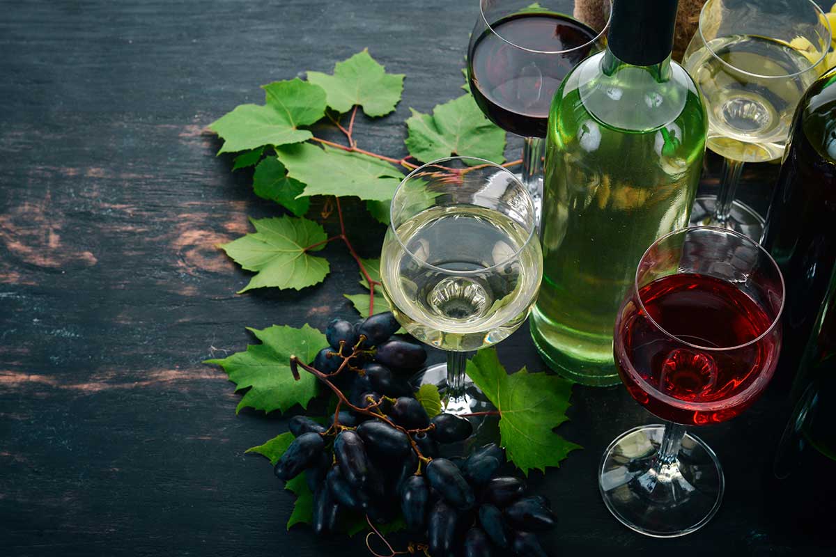 A selection of wine bottles and glasses, with fresh grapes and leaves, illustrating the natural origin of terpenes in wine.