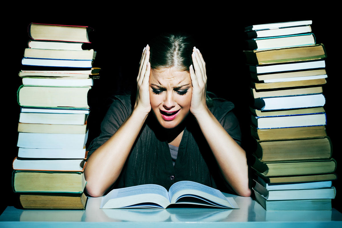 A woman sitting on a desk with two big piles of books is  having a hard time working and needs terpenes for focus and concentration.